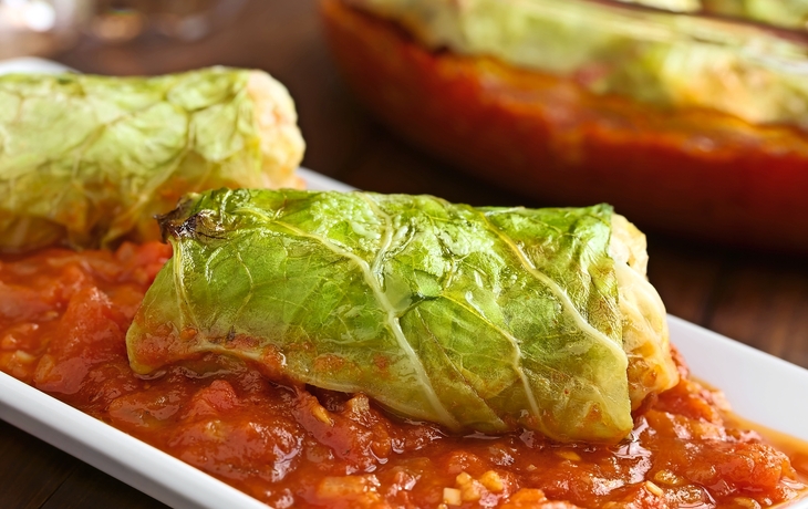 Vegetarische Kohlroulade gefüllt mit Reis, Paprika, Zwiebel und Karotte, serviert auf Tomatensauce, fotografiert mit natürlichem Licht (Selektiver Fokus, Fokus auf die Vorderseite der Roulade)